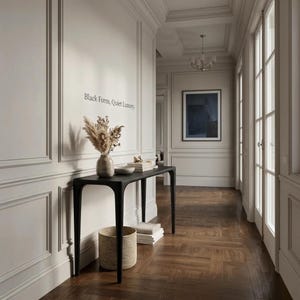 Puede incluir: Una mesa consola negra de cuatro patas delgadas se apoya contra una pared con paneles que presenta el texto Black Form, Quiet Luxury. Sobre la mesa hay un jarr&oacute;n de cer&aacute;mica con hierbas secas y una pila de libros, con una cesta tejida debajo.