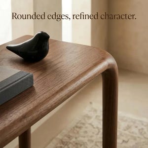 Peut inclure: Une table en bois aux bords arrondis et au grain lisse. Une figurine d'oiseau noire est pos&eacute;e sur la surface &agrave; c&ocirc;t&eacute; d'un objet rectangulaire gris. Le texte "Rounded edges, refined character." est inscrit en haut de l'image.