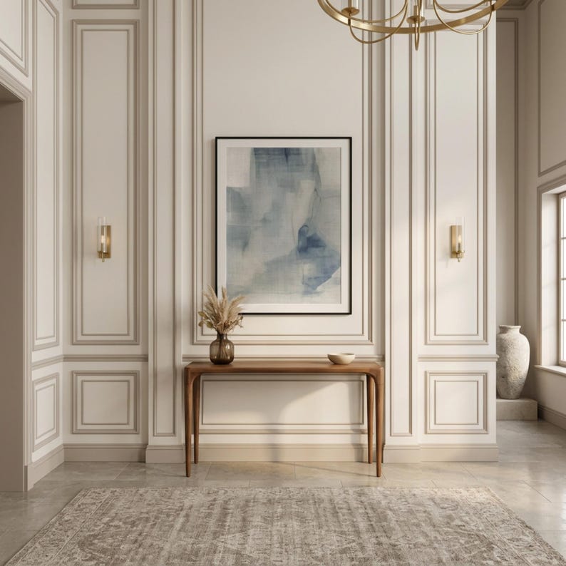 May include: An interior hallway with a neutral color palette. A framed abstract painting in shades of blue and white hangs above a wooden console table. A vase with dried plants and a small bowl are on the table. A patterned rug covers the floor.