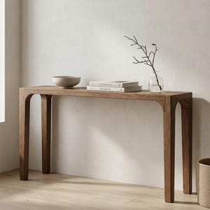 Puede incluir: Una mesa consola rectangular de madera con patas arqueadas y acabado de veta lisa. Sobre la superficie hay un cuenco beige poco profundo, dos libros apilados con cubiertas blancas y un jarrón de cristal transparente con una rama fina.