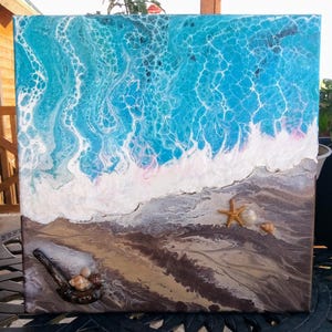 May include: Square canvas art depicting an ocean scene. The top half shows a vibrant blue ocean with white foamy waves. The bottom half features a sandy beach with seashells and a starfish. The artwork has a textured, layered appearance.