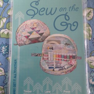 May include: A teal blue sewing pattern with the title "Sew on the Go" and the text "#401 GET IT ALL TOGETHER". The pattern features a quilted fabric pouch with a zipper and a clear plastic pouch with a zipper. The pattern also includes contact information for Timber Lane.
