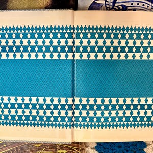 May include: Open book with a teal and cream geometric pattern. The design features rows of white diamonds and teal diamond patterns. The book is open, revealing the interior pages with the same design.