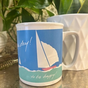 May include: White ceramic mug with a blue and green design featuring a sailboat and the text "It's a day! ... to be happy!"