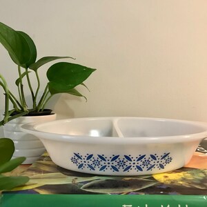 Puede incluir: Un plato para hornear blanco dividido con un patrón floral azul. El plato está sobre una pila de libros de cocina.