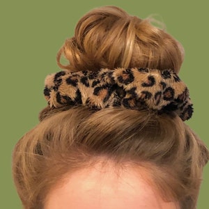 Puede incluir: Un scrunchie para el pelo de color marrón y negro con estampado de leopardo.