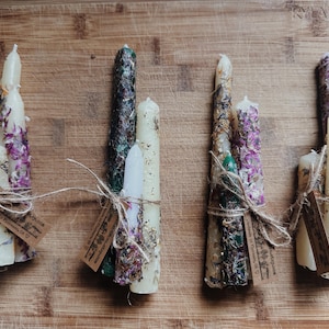 Puede incluir: Conjunto de cuatro velas artesanales con flores y hierbas secas incrustadas en la cera. Las velas están atadas con cuerda y tienen una estética rústica.