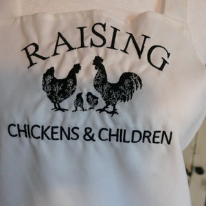 May include: White kitchen apron with black embroidery that reads "Raising Chickens & Children" with a rooster and two hens and chicks.