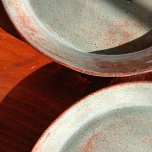May include: Two handmade ceramic serving platters. The plates have a light green speckled glaze with a reddish-brown rim. The plates are oval-shaped and appear to be on a wooden surface.