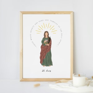 May include: Framed art print featuring an illustration of St. Lucy. The artwork depicts a woman in a green dress and red shawl, holding a book and a palm branch. The text reads "Those whose hearts are pure are temples of the Holy Spirit."