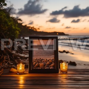 May include: A framed photograph of a beach scene with rocks and water, sitting on a wooden surface with two lit candles on either side.