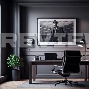 May include: A dark gray home office with a large window, a desk with a laptop, a black leather office chair, a black and white framed photo of a man in a suit and hat, a potted plant, and a desk lamp.