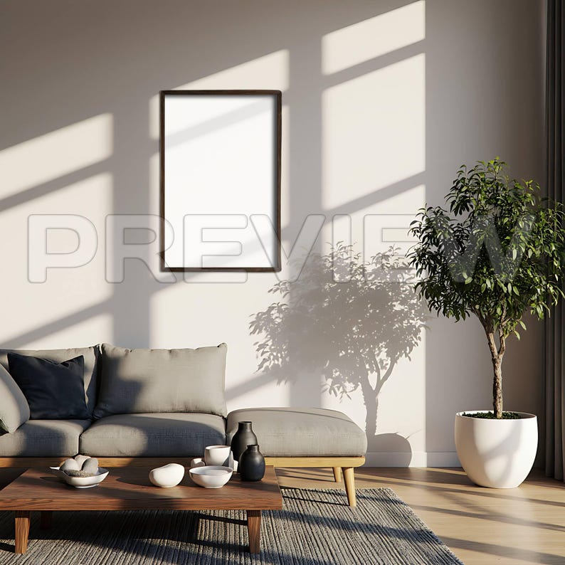 May include: A modern living room scene with a gray sofa, ottoman, and wooden coffee table. A framed blank print hangs on the wall. Decorative bowls and vases are on the table. A potted plant sits in the corner, and sunlight casts shadows.