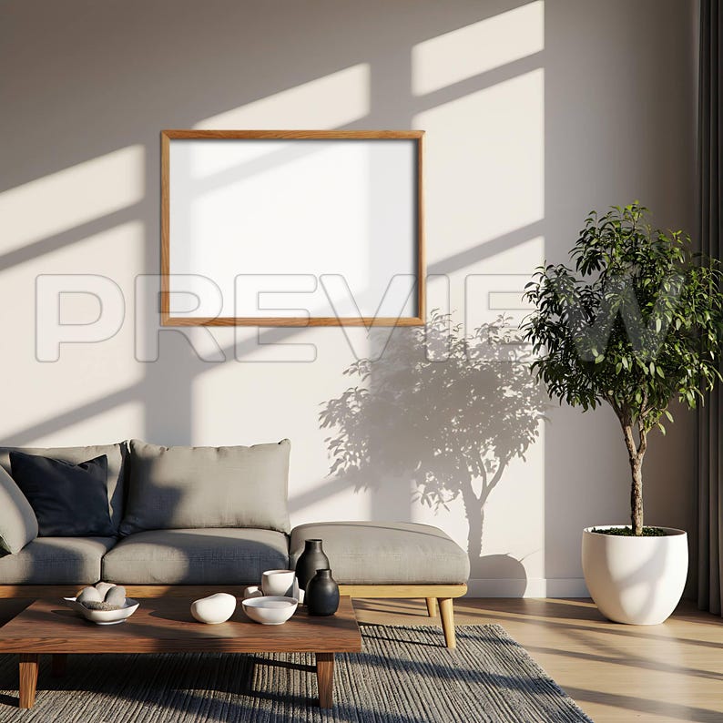 May include: A living room scene featuring a wooden-framed blank picture on a white wall. A gray sofa, ottoman, and wooden coffee table are in front of the wall. A potted plant sits to the right, and sunlight casts shadows.