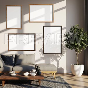May include: Four framed art pieces with white interiors are mounted on a light-colored wall. The frames are in various sizes and colors, including light and dark wood. A sofa, ottoman, and coffee table are in the foreground, with a potted plant to the right.