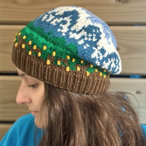 May include: A knitted beanie hat with a colorful design. The hat features a brown base, a green and blue midsection, and a white and blue patterned top. Yellow dots are incorporated into the design. The hat is made of soft yarn.