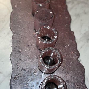 May include: A set of five clear glass candle holders with silver glitter accents. The holders are arranged in a row on a pink and silver speckled surface.