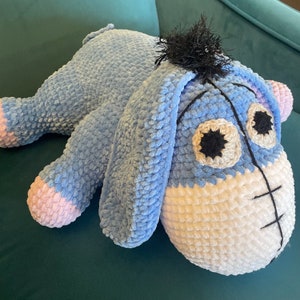 May include: A blue and white crocheted stuffed animal resembling a donkey. The animal has a long snout, large ears, and a fluffy tail.