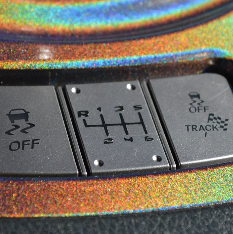 May include: Close-up of a car's gear shift panel with buttons labeled "OFF", "TRACK", and a gear shift pattern with numbers 1 through 6 and the letter "R".