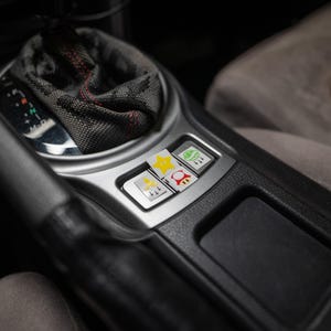 Pu&ograve; includere: Dettaglio degli interni dell'auto con coperture personalizzate dei pulsanti del cambio. Le coperture presentano grafiche colorate di una stella gialla, un fungo rosso, una foglia verde e un razzo. I pulsanti sono inseriti in una finitura argentata.