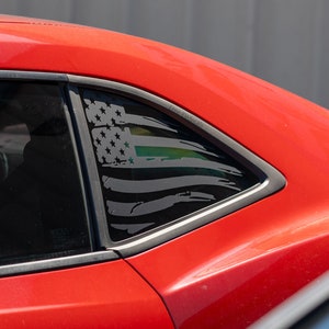 Può includere: Un'auto rossa con un adesivo della bandiera americana in bianco e nero sul lunotto posteriore. La bandiera ha una sottile linea verde.