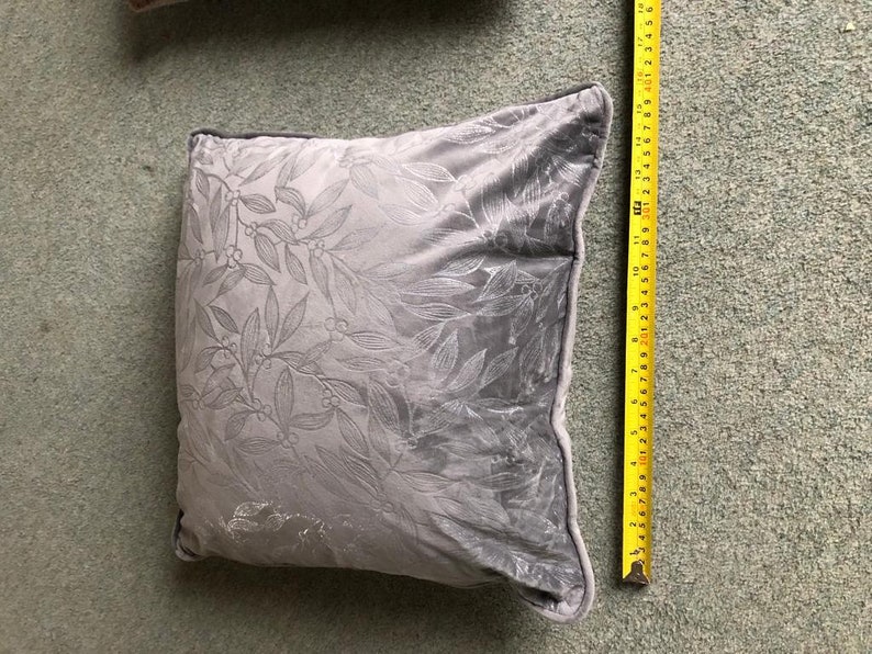 May include: A gray velvet pillow with a white floral pattern. The pillow is approximately 18 inches long.