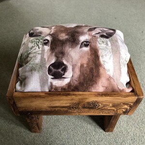 May include: A wooden stool with a deer print cushion. The stool has a rustic brown finish and three legs.
