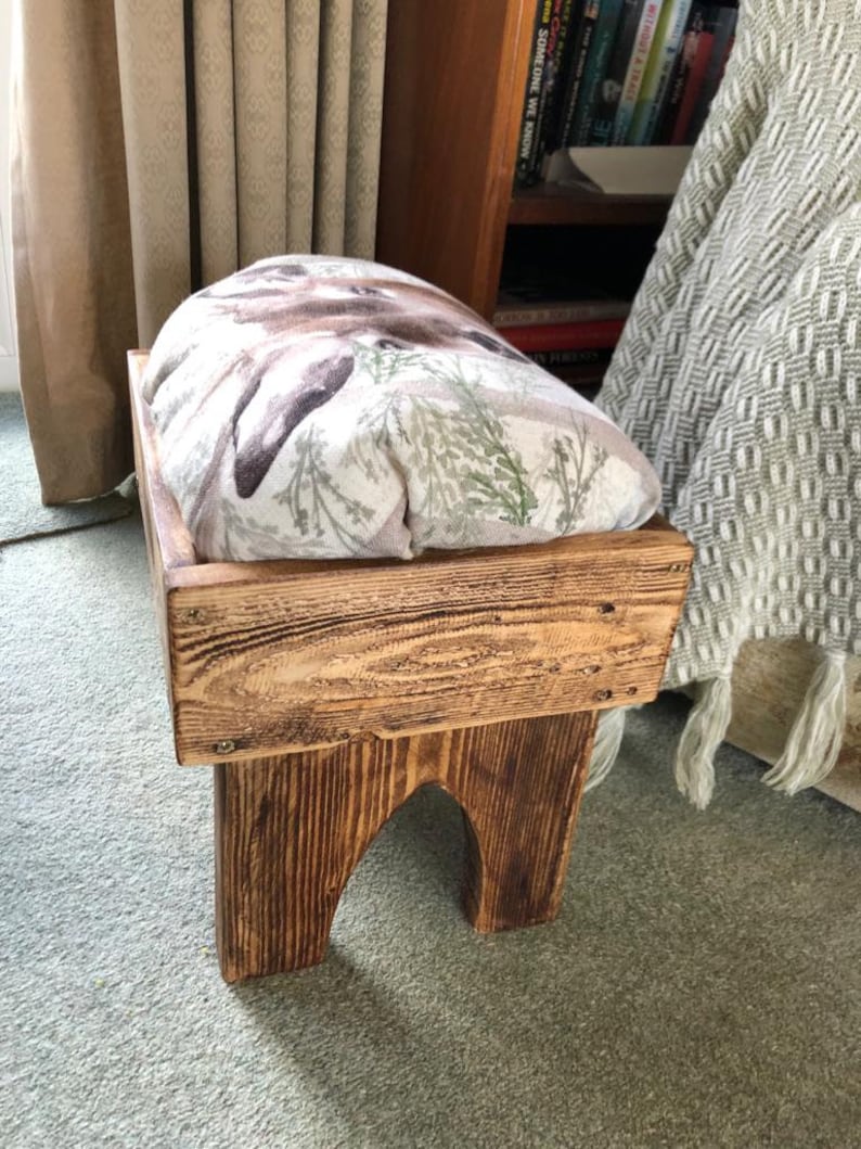 May include: A wooden footstool with a padded top featuring a floral and animal print. The footstool has a rustic brown finish and is made of reclaimed wood.