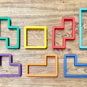 May include: A collection of colorful, geometric shapes in various colors, including green, yellow, red, blue, purple, and orange. The shapes are arranged on a wooden surface, resembling Tetris game pieces. These are likely cookie cutters or craft supplies.