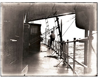 May include: A black and white photo of a man standing on the deck of a ship. The man is wearing a light-colored shirt and is looking out at the sea. The ship is in the middle of the ocean, and the waves are crashing against the side of the ship.