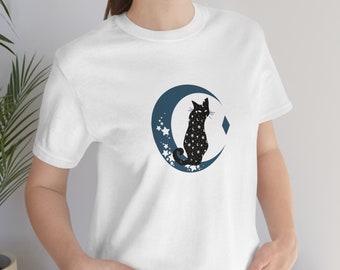 Op de afbeelding: Wit T-shirt met een zwarte kat die op een blauwe halve maan zit. De kat is bedekt met witte sterren.