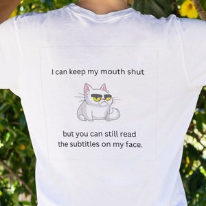 May include: White t-shirt with a cartoon cat and the text "I can keep my mouth shut but you can still read the subtitles on my face."
