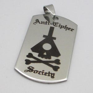 May include: A silver metal dog tag pendant with a black and white image of a skull and crossbones. The text "Anti-Cipher Society" is engraved on the tag.