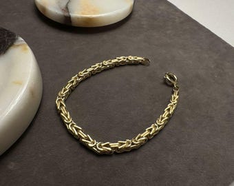 May include: A gold chain bracelet with a byzantine style link pattern.