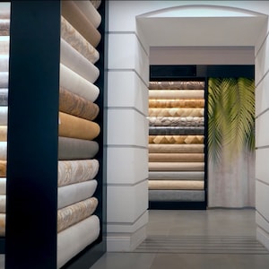 K&ouml;nnte beinhalten: Eine Wand mit Regalen, die mit Rollen von Tapeten in verschiedenen Farben und Mustern gef&uuml;llt sind. Die Regale sind in einem Raster angeordnet und die Tapeten sind ordentlich gestapelt. Die Tapeten sind in verschiedenen Texturen und Farben, darunter Beige, Braun, Grau und Wei&szlig;.