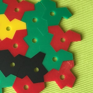 May include: A close-up of a colourful geometric puzzle made of interlocking pieces in red, green, black, and yellow. The puzzle pieces are arranged in a pattern on a green background.