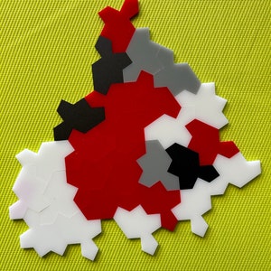 May include: A geometric puzzle made of red, white, black, and grey plastic pieces. The pieces are arranged in a triangular shape.