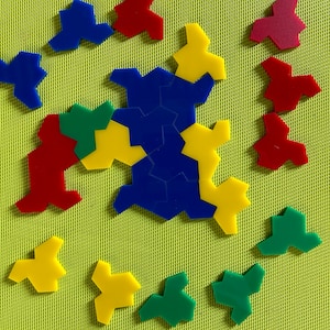 May include: A set of colourful geometric puzzle pieces in red, blue, green, and yellow. The pieces are arranged in a pattern on a green surface.