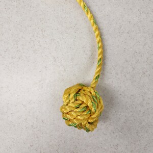 May include: A yellow and green rope toy for dogs. The rope is tied into a knot at both ends, creating a ball shape.