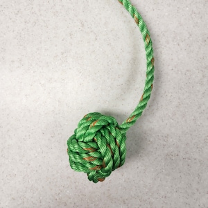 May include: Green and brown rope toy with a knotted ball on each end.