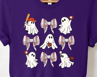 May include: A purple short-sleeve t-shirt featuring a graphic print of four white ghosts and three bows. The ghosts are depicted with baseball gear, including caps and gloves, while the bows feature a red-stitched baseball pattern design.