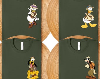 May include: Six green t-shirts with different Disney characters wearing safari outfits. The characters are Donald Duck, Goofy, Pluto, Mickey Mouse, and Minnie Mouse. The t-shirts are numbered 1 through 6.