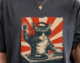 May include: Dark gray t-shirt featuring a graphic of a cat DJ wearing sunglasses and headphones, with a red and white striped background. The cat is positioned behind a turntable, with one paw raised.
