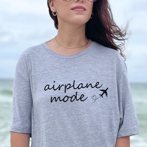 K&ouml;nnte beinhalten: Ein graues T-Shirt mit dem Text "Flugzeugmodus" und einer kleinen Flugzeuggrafik.