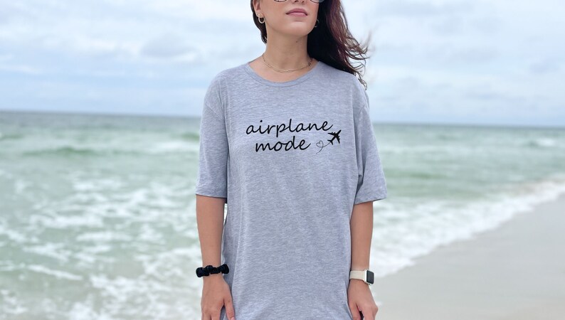K&ouml;nnte beinhalten: Ein graues T-Shirt mit dem Text "Flugzeugmodus" und einer kleinen Flugzeuggrafik.