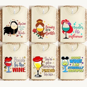 May include: Six cream-colored t-shirts with wine-themed graphics. Designs include wine glasses with text like "Can you Drink all the Colors of the Wine", "Beauty and the Bottle", and "Ooooh Wine! I am Eternally Grateful!"
