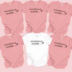 K&ouml;nnte beinhalten: F&uuml;nf T-Shirts mit dem Text "Flugzeugmodus" und einer kleinen Flugzeuggrafik. Vier der Shirts sind rosa und eines ist wei&szlig;.