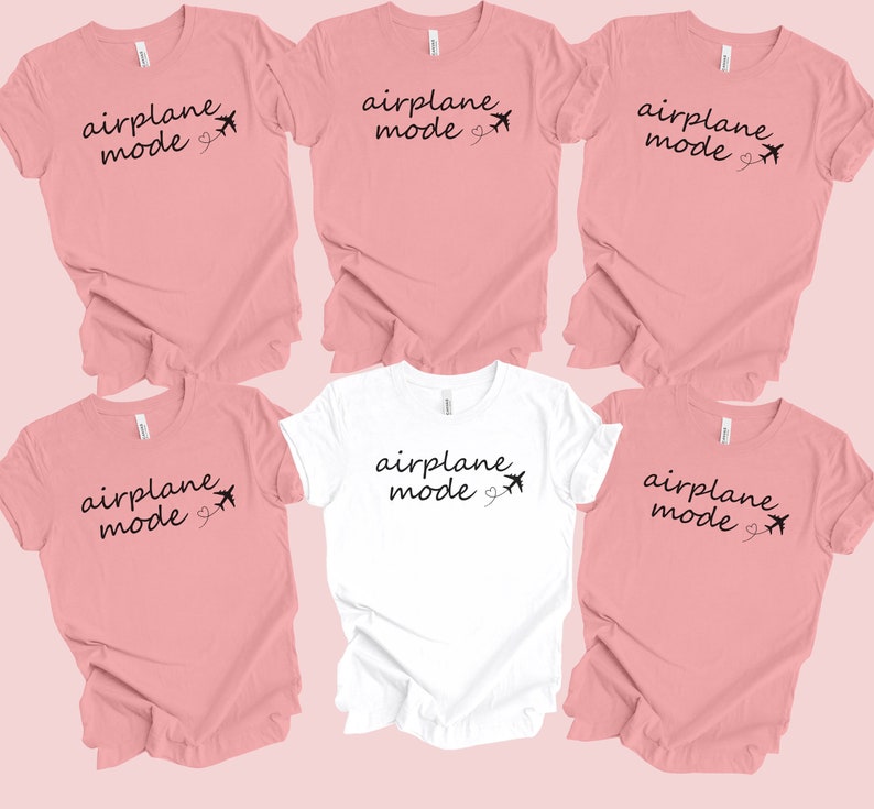 K&ouml;nnte beinhalten: F&uuml;nf T-Shirts mit dem Text "Flugzeugmodus" und einer kleinen Flugzeuggrafik. Vier der Shirts sind rosa und eines ist wei&szlig;.