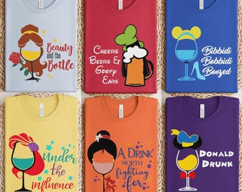 May include: Six t-shirts in light blue, red, blue, yellow, orange, and purple. Each features a graphic of a wine glass or beer mug with character-themed elements and text including Beauty and the Bottle, Cheers Beers & Goofy Ears, Bibbidi Bobbidi Boozed, Under the Influence, A Drink Worth Fighting For, and Donald Drunk.