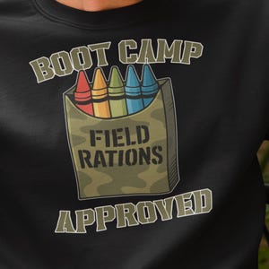 May include: Black sweatshirt with the text "BOOT CAMP FIELD RATIONS APPROVED." The graphic features a box of crayons in red, orange, yellow, green, and blue. The sweatshirt is a crew neck style.
